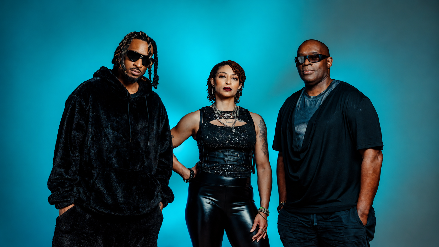 Dantiez Saunderson, Steffanie Christi’an and Kevin Saunderson posing together against a blue studio background