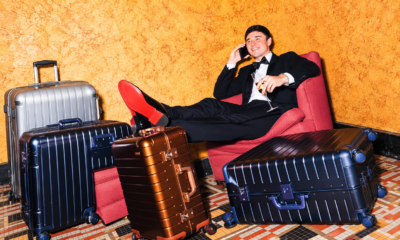 ohn Summit sitting in a red chair surrounded by aluminum suitcases for his Away partnership campaign