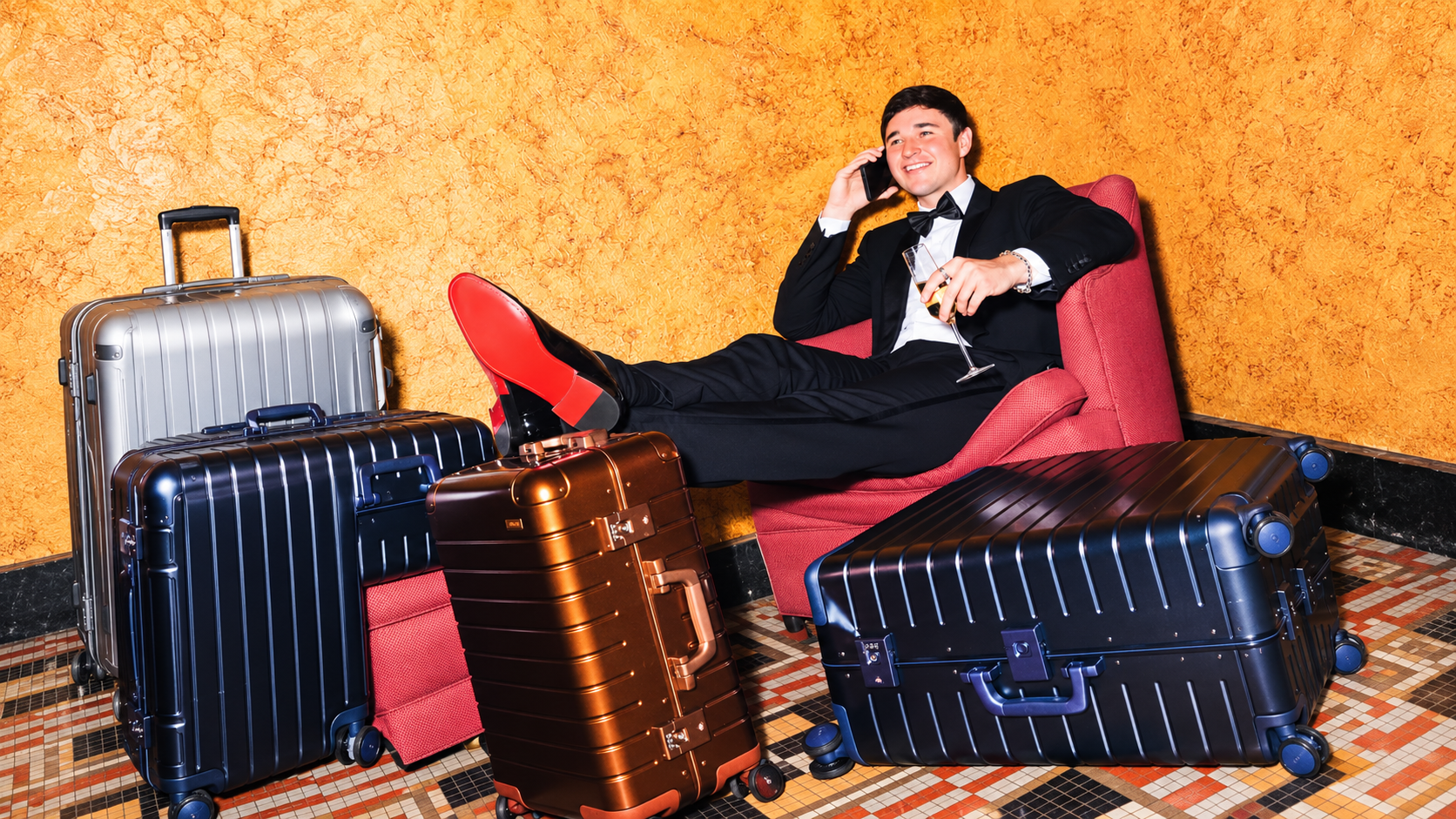 ohn Summit sitting in a red chair surrounded by aluminum suitcases for his Away partnership campaign
