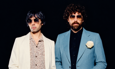 ustice duo posing in sunglasses against a black background, wearing white and blue suits