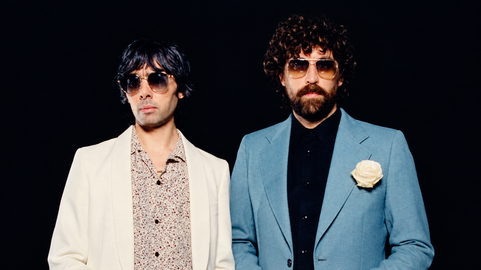 ustice duo posing in sunglasses against a black background, wearing white and blue suits