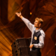Lost Frequencies smiling on stage with his arm raised during a performance under warm orange lighting