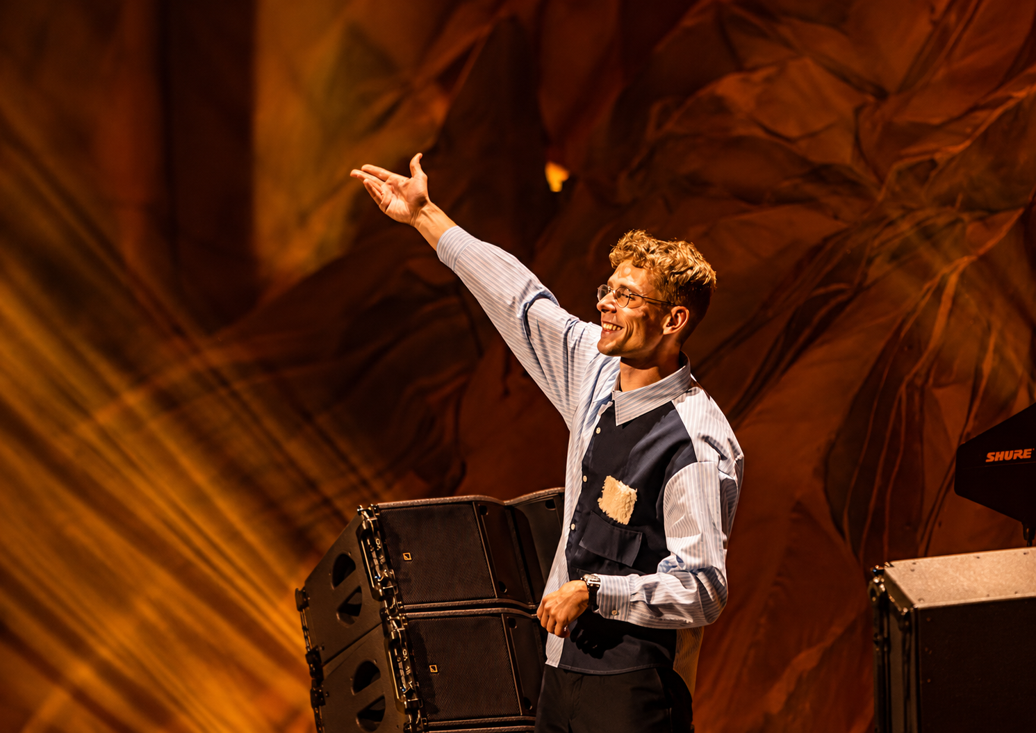 Lost Frequencies smiling on stage with his arm raised during a performance under warm orange lighting