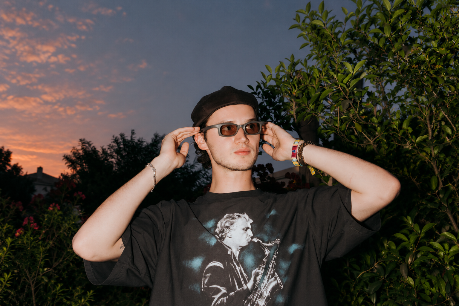 Mau P wearing sunglasses and a black cap outdoors at sunset