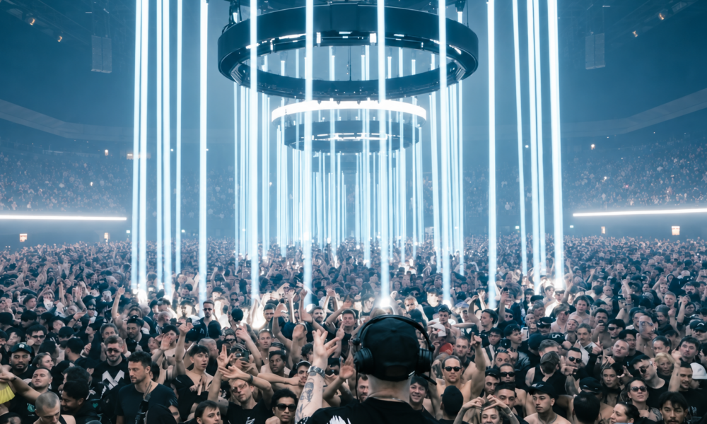 Klangkuenstler performing to a large crowd at an OUTWORLD show beneath vertical white light installations.