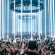 Klangkuenstler performing to a large crowd at an OUTWORLD show beneath vertical white light installations.