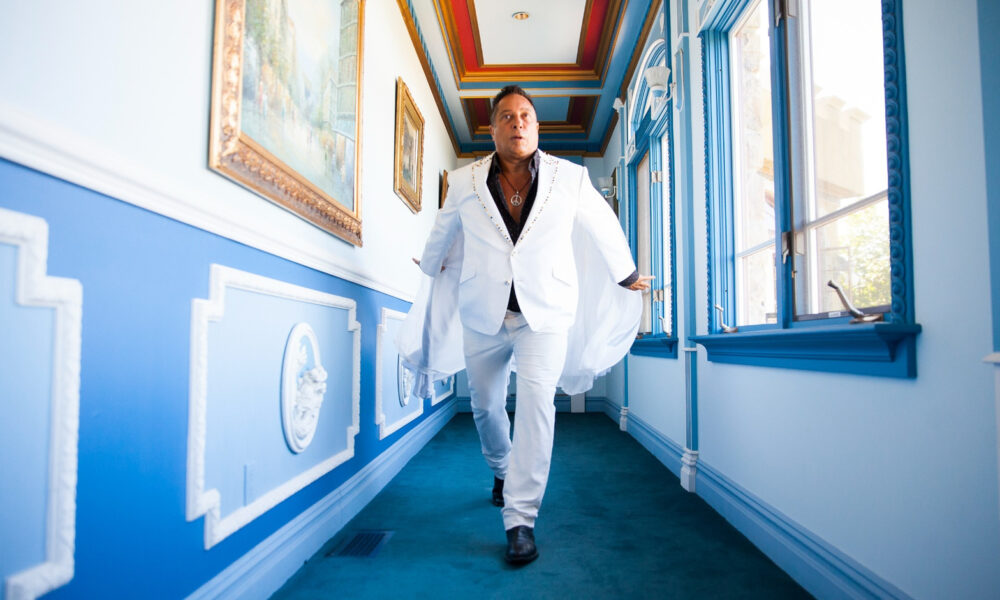 Sir Ivan wearing a white suit while walking through a blue and white hallway