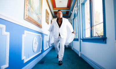 Sir Ivan wearing a white suit while walking through a blue and white hallway