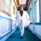 Sir Ivan wearing a white suit while walking through a blue and white hallway