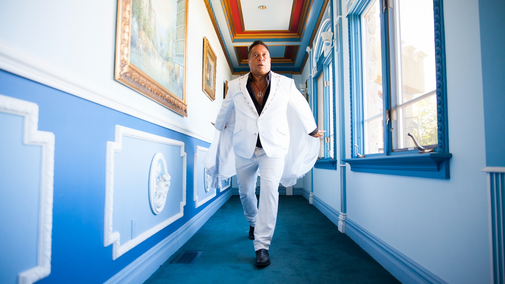 Sir Ivan wearing a white suit while walking through a blue and white hallway