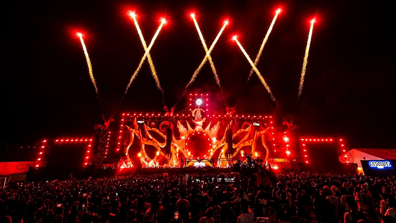 Sunburn Festival stage glowing red as fireworks launch above a large nighttime crowd.