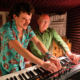Woody Cook and Zed Bias working together on a synthesizer inside a recording studio